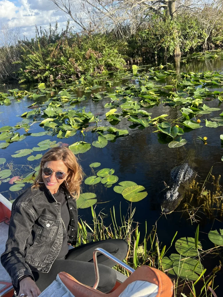 Guest seated on an airboat with an alligator in the lily pads just beside the boat