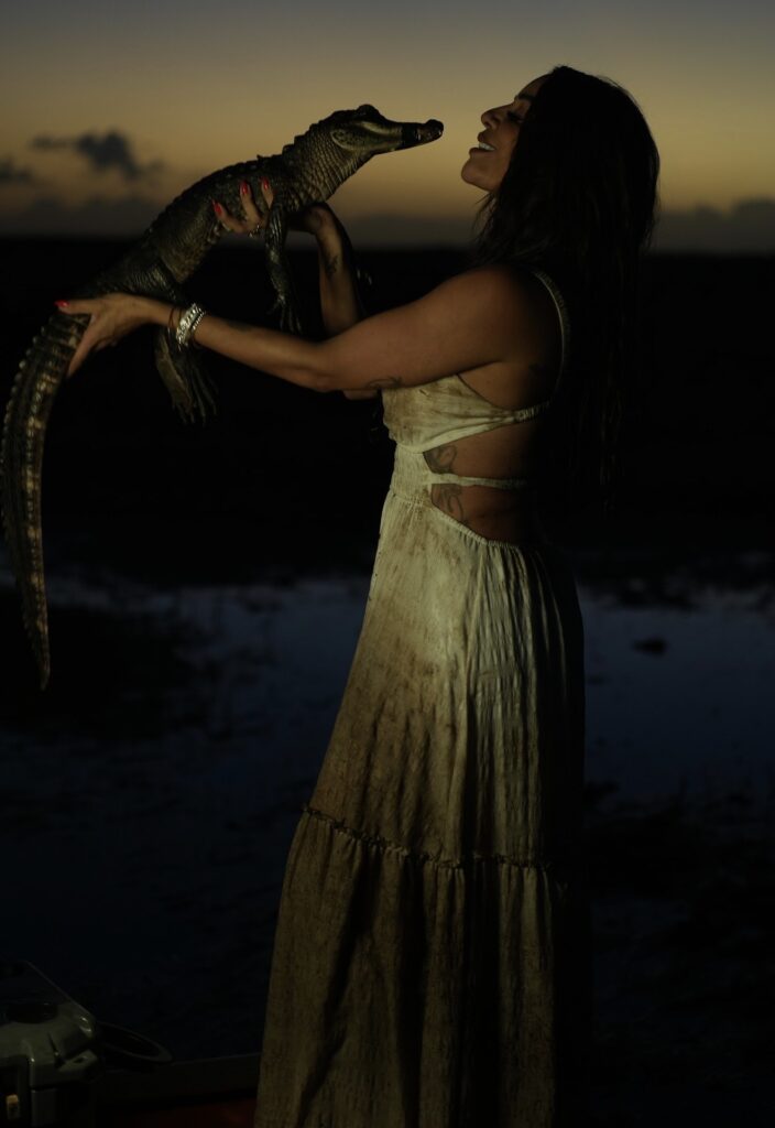 Woman in a long dress holding a small alligator at dusk