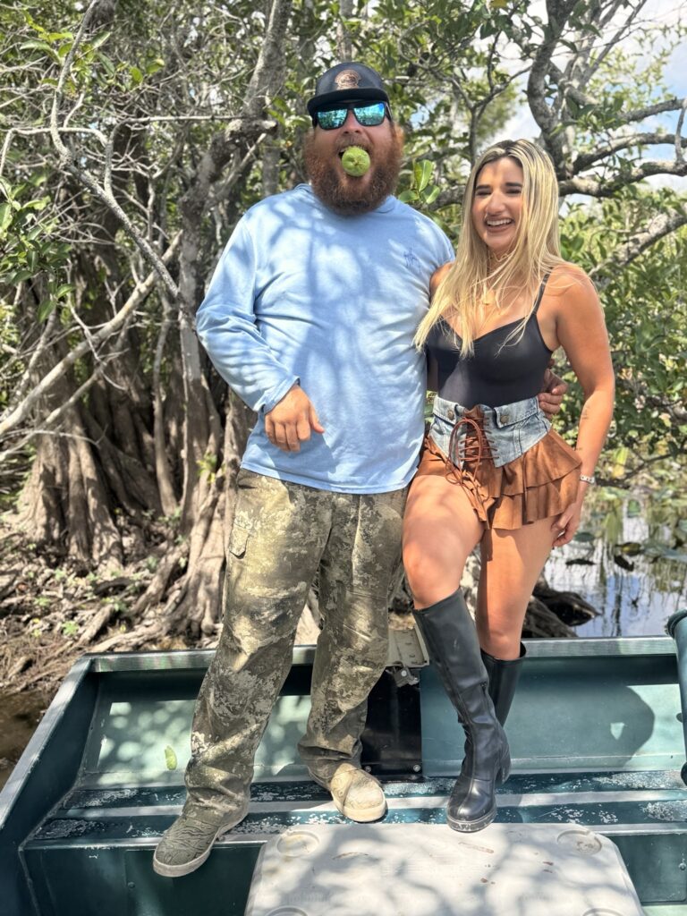 Two adults posing on a boat beside trees in the wetlands