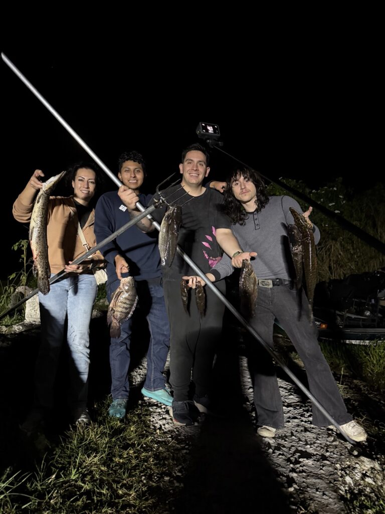 Four guests displaying fish and gigging poles at night