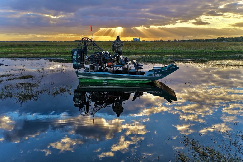 Airboat reflected in calm water beneath sunlit clouds