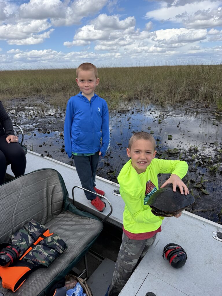 Two children aboard an airboat with a turtle