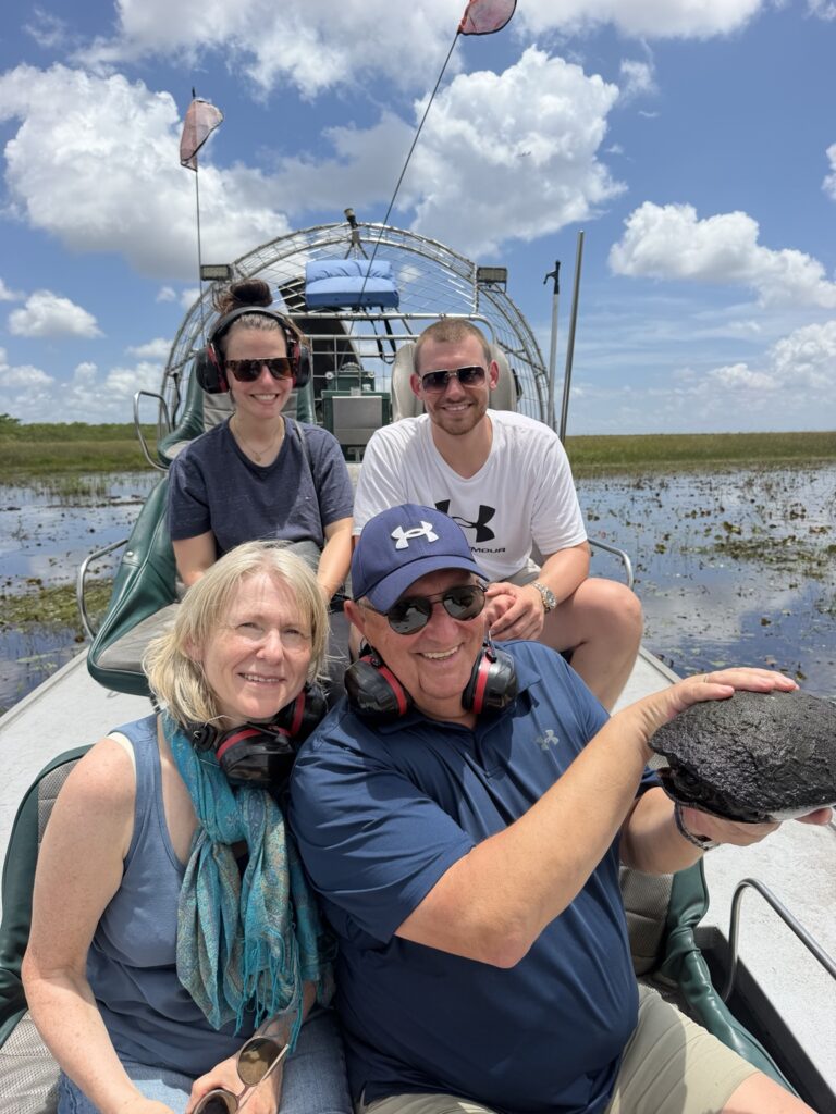 Four smiling guests on an airboat with one holding a turtle