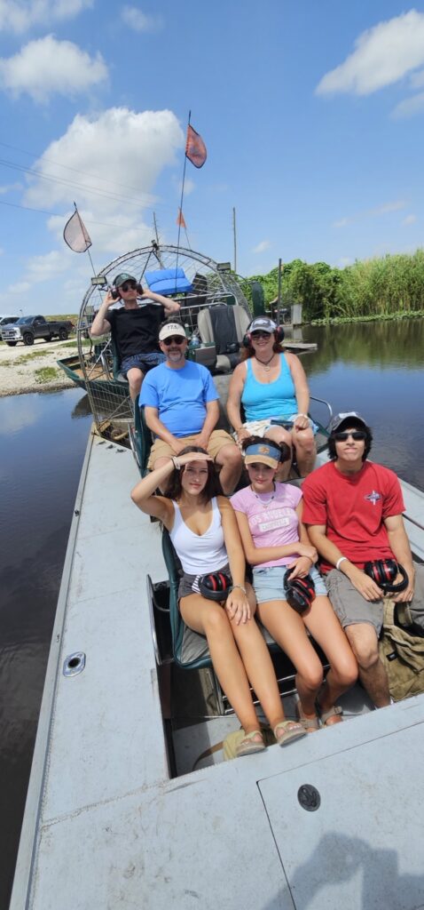 Six guests seated on an airboat beside the water