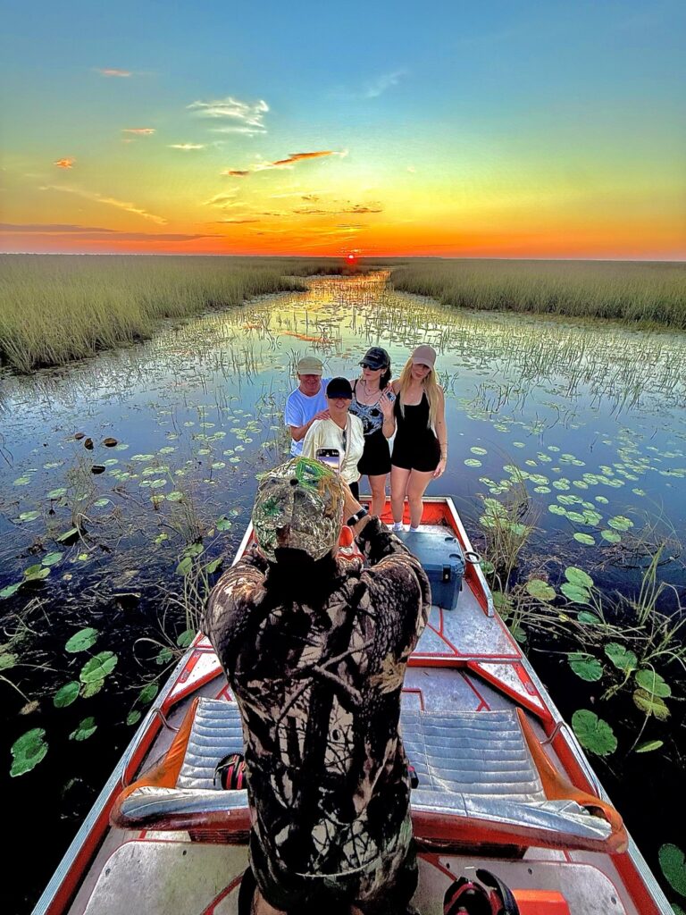 Group posing on an airboat as a photographer captures the sunset